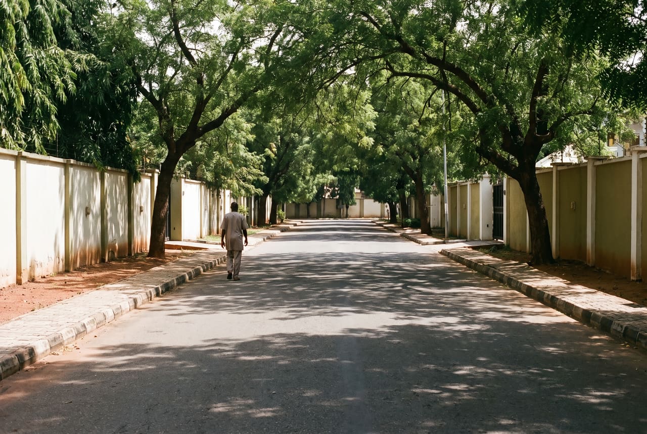 A tree-lined street in Maitama, Abuja, in midday shade with one person walking away